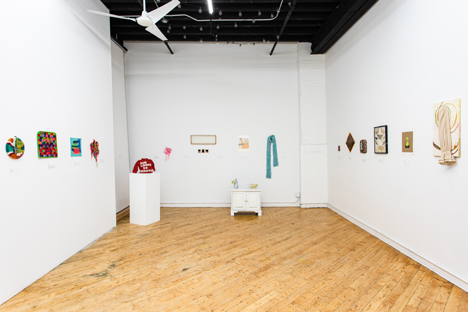 A room with small textile artworks hanging on white walls
