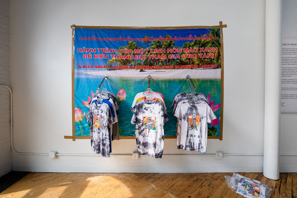 A site-specific installation resembling the interior space of a clothing store. Across a series of beach and tropical-themed retail displays are t-shirts that are available for purchase.