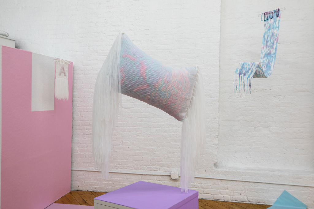 A rectangular throw-sized transparent pillow stuffed with pink, purple, green and orange yarn snips suspended at an angle with soft tulle yarn fringe falling from both ends.