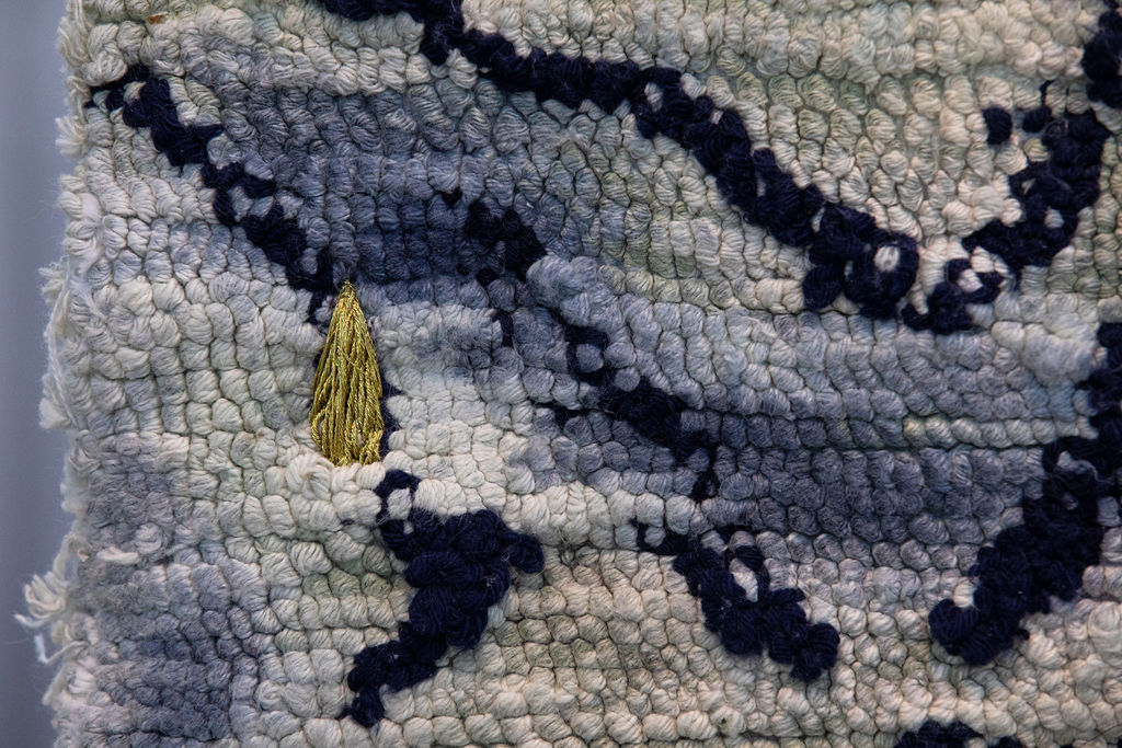 Detailed shot of stitch work by Cong-Tam Nguyen using various hues of navy blue and white and gold stitching in the shape of a small tear drop on the left side of the image.