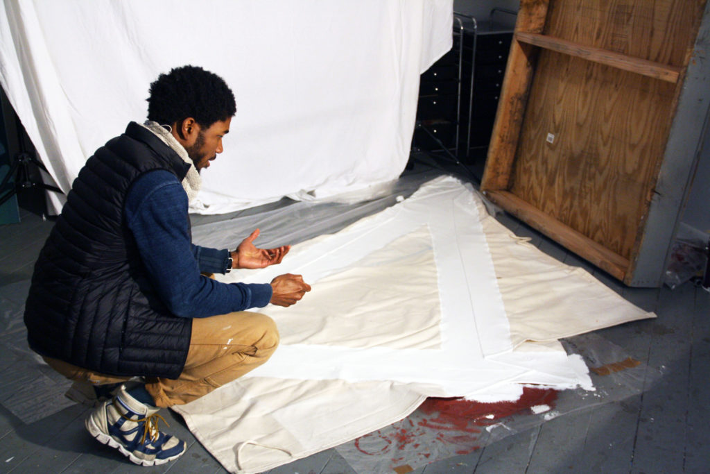 Ryan crouches in front of a spread of white cloth on the floor