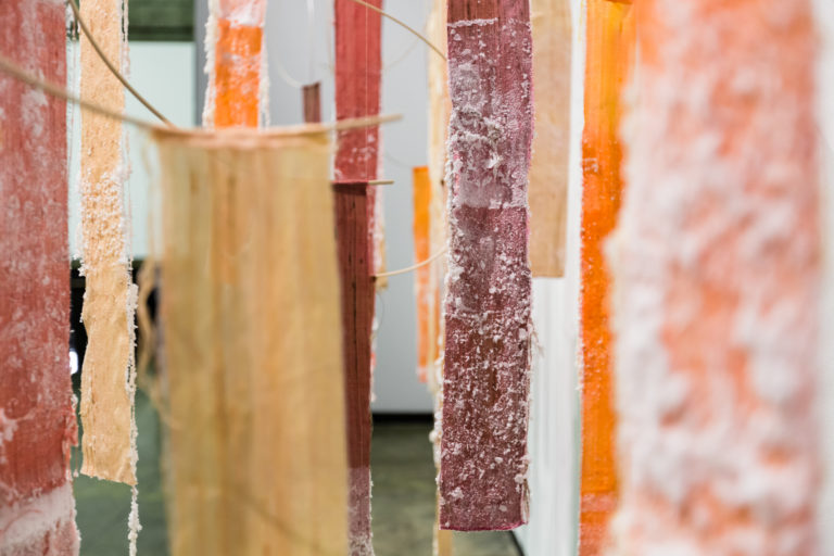 A gallery space filled with pieces of handmade paper in organic shapes in fleshy pink and cream colours.